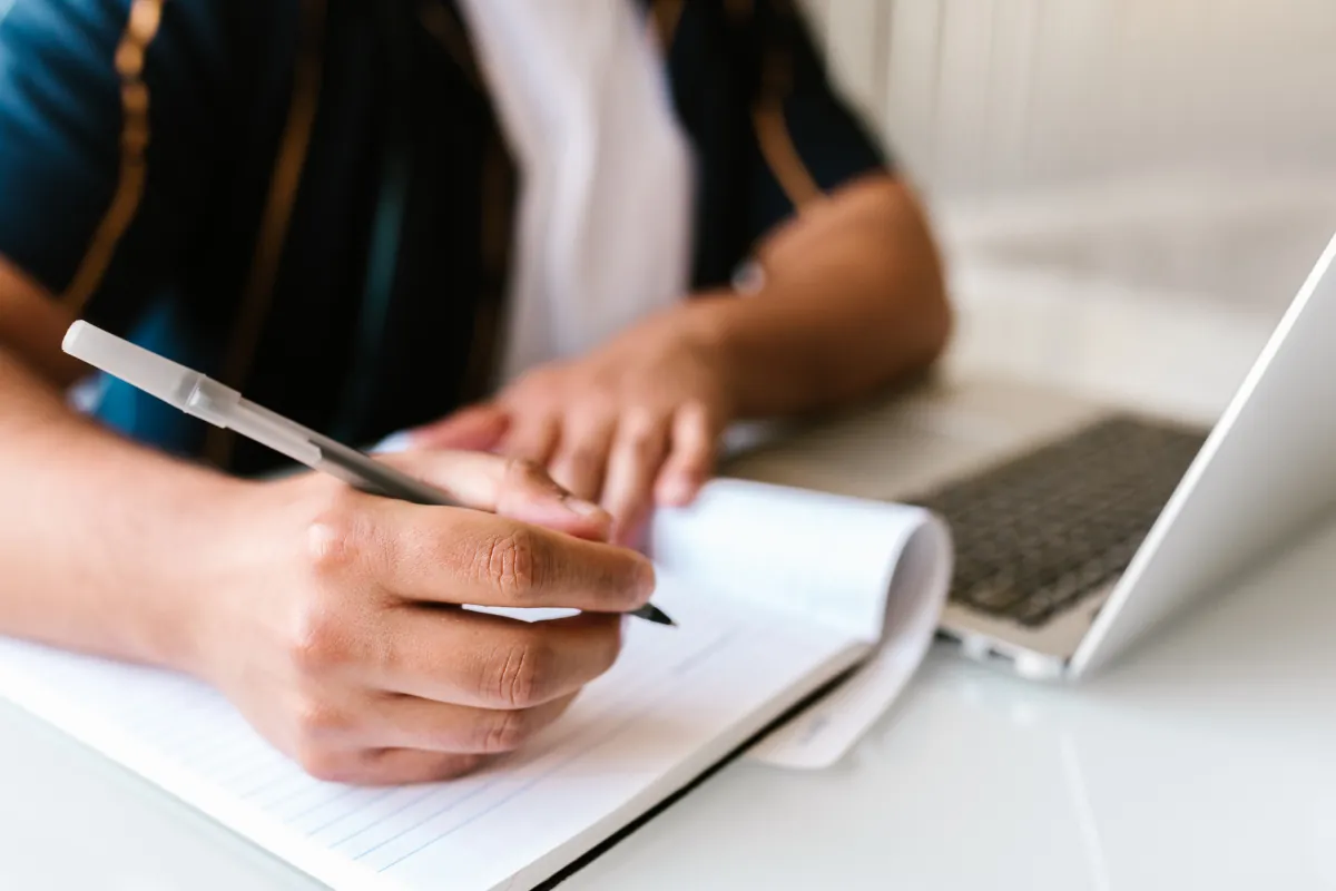  Pessoa escrevendo anotações enquanto estuda online com notebook