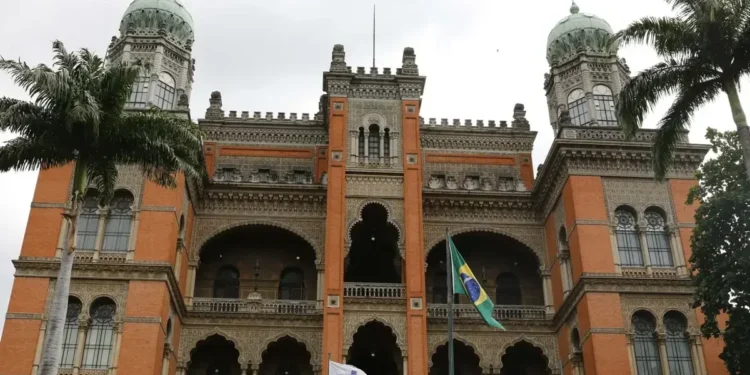 Imagem do prédio histórico da Fiocruz, com suas características arquitetônicas marcantes e bandeiras do Brasil e do SUS ao fundo.