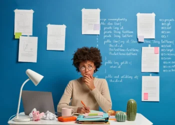 Mulher pensativa estudando código e anotações em uma parede azul, refletindo sobre o plural de férias