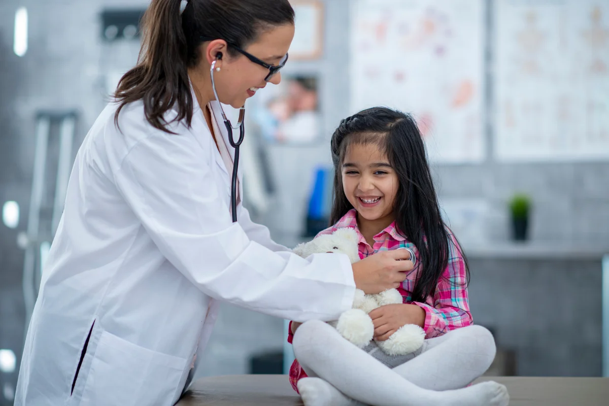 Médica examinando uma criança sorridente em consulta pediátrica.