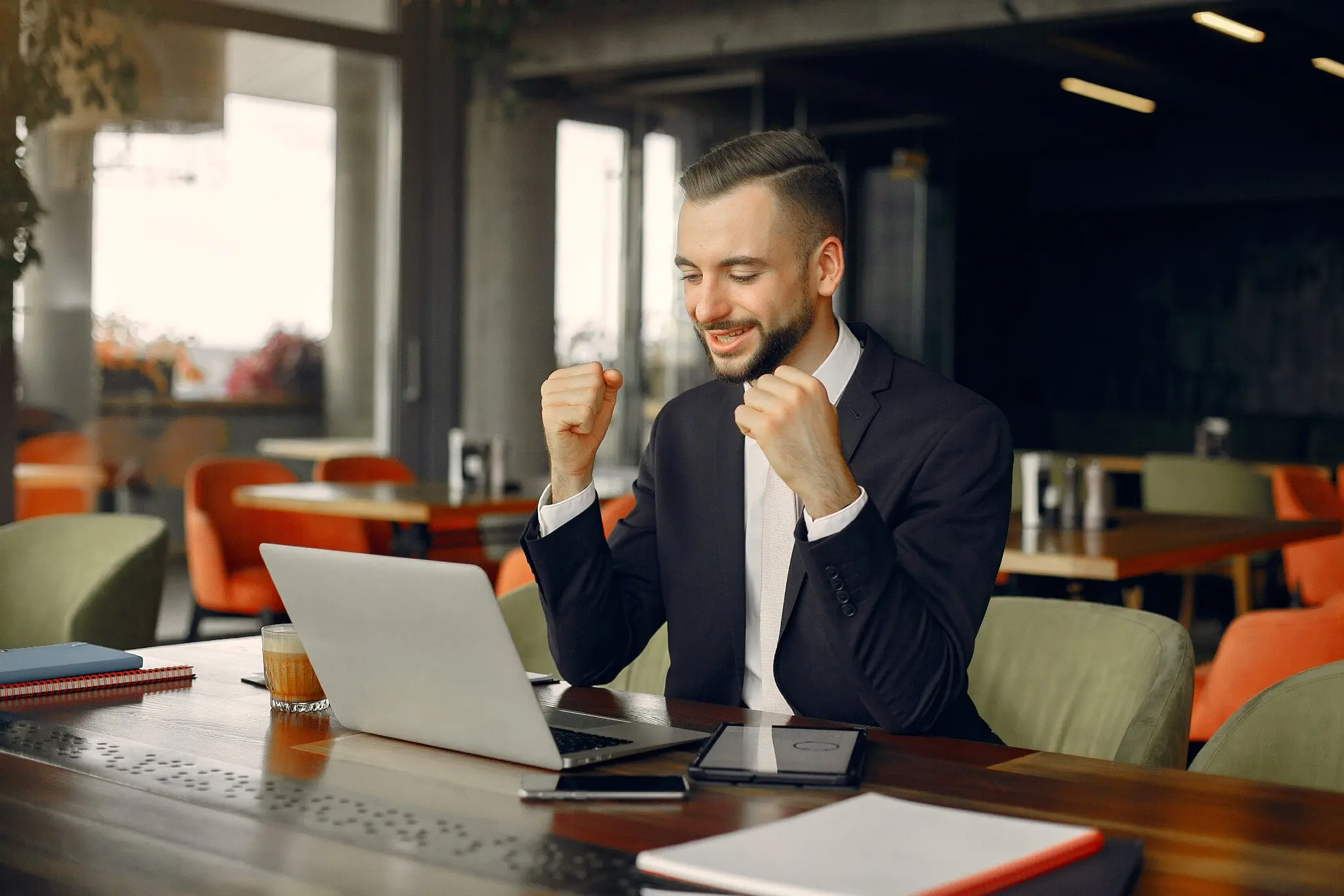 Empreendedor comemorando sucesso em seu escritório com laptop à frente.