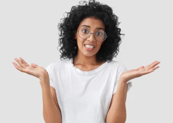 Mulher de cabelos cacheados com expressão de dúvida e as mãos abertas.