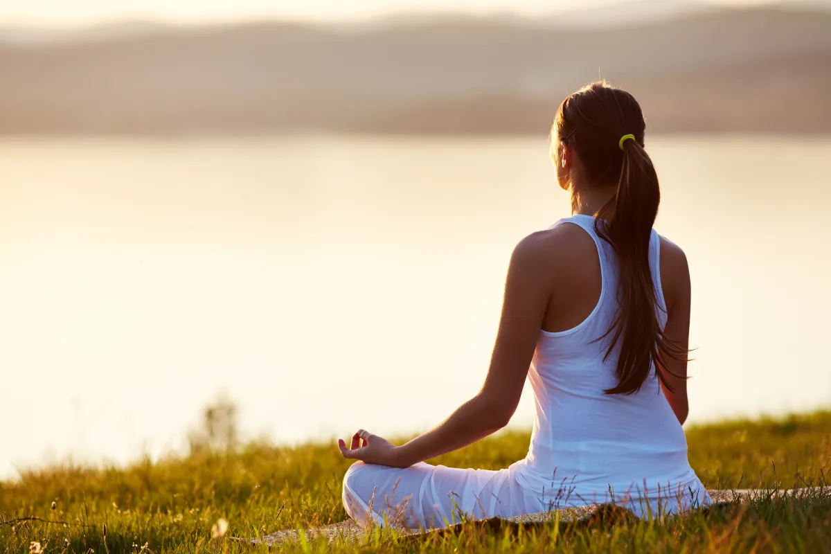 Mulher praticando meditação ao ar livre durante o amanhecer.