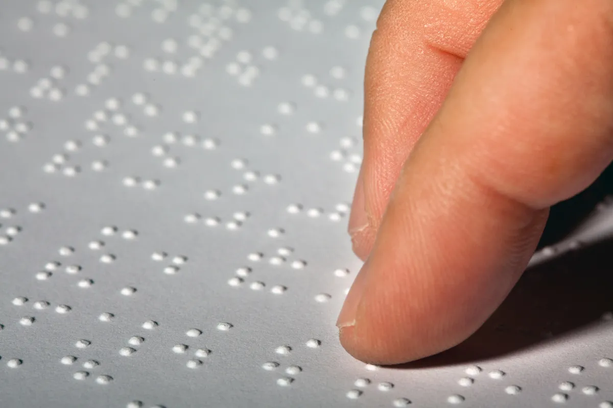 Pessoa lendo Braille com a ponta dos dedos sobre o papel.