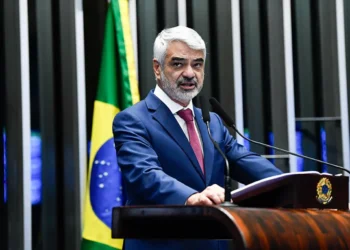 Senador Humberto Costa discursando no plenário do Senado, com a bandeira do Brasil ao fundo.