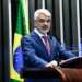 Senador Humberto Costa discursando no plenário do Senado, com a bandeira do Brasil ao fundo.
