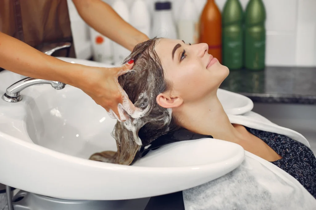 Profissional lavando o cabelo de uma cliente em salão de beleza, destacando a área de estética