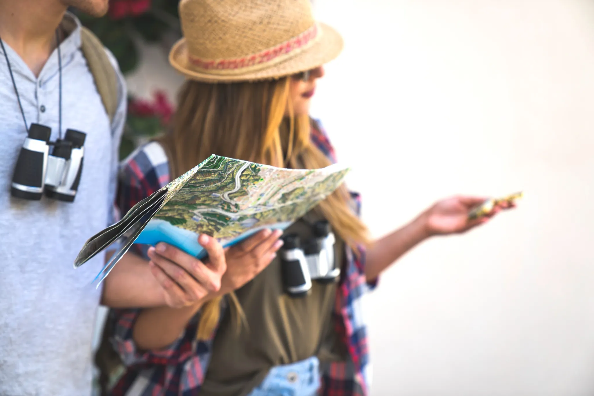 Casal jovem explorando um mapa durante uma viagem ao ar livre, ambos com binóculos pendurados no pescoço.