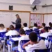 Alunos do ensino fundamental em aula de inglês com professora no quadro.