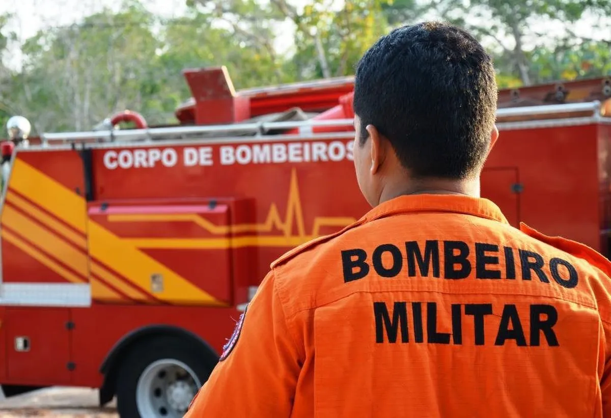 Bombeiro militar de uniforme laranja em frente a viatura do Corpo de Bombeiros.