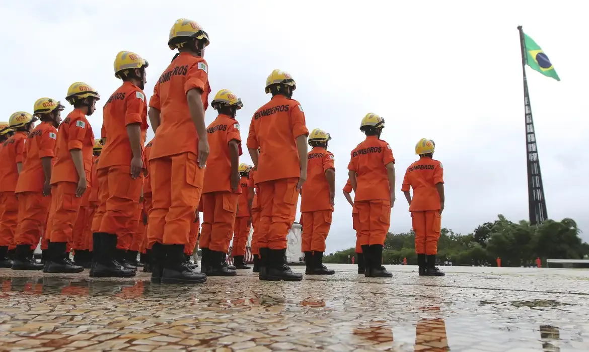 Cerimônia de formatura de bombeiros em frente à bandeira do Brasil.