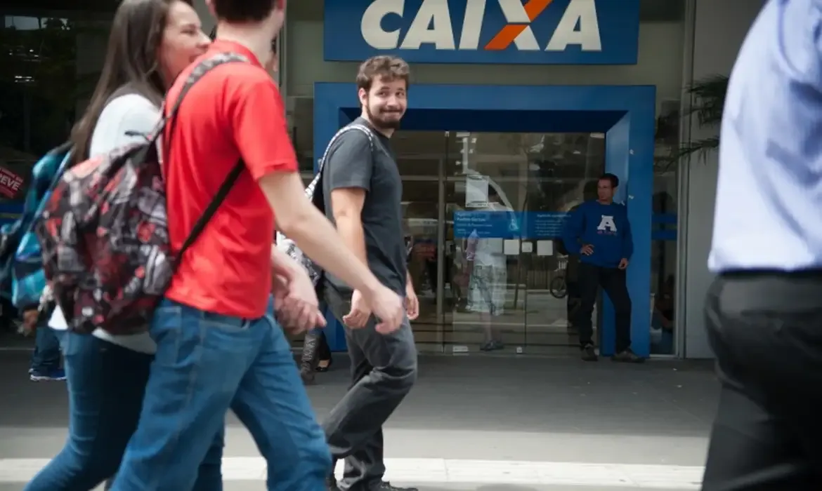 Clientes caminhando em frente à agência da Caixa Econômica Federal, com destaque para o logo da instituição.