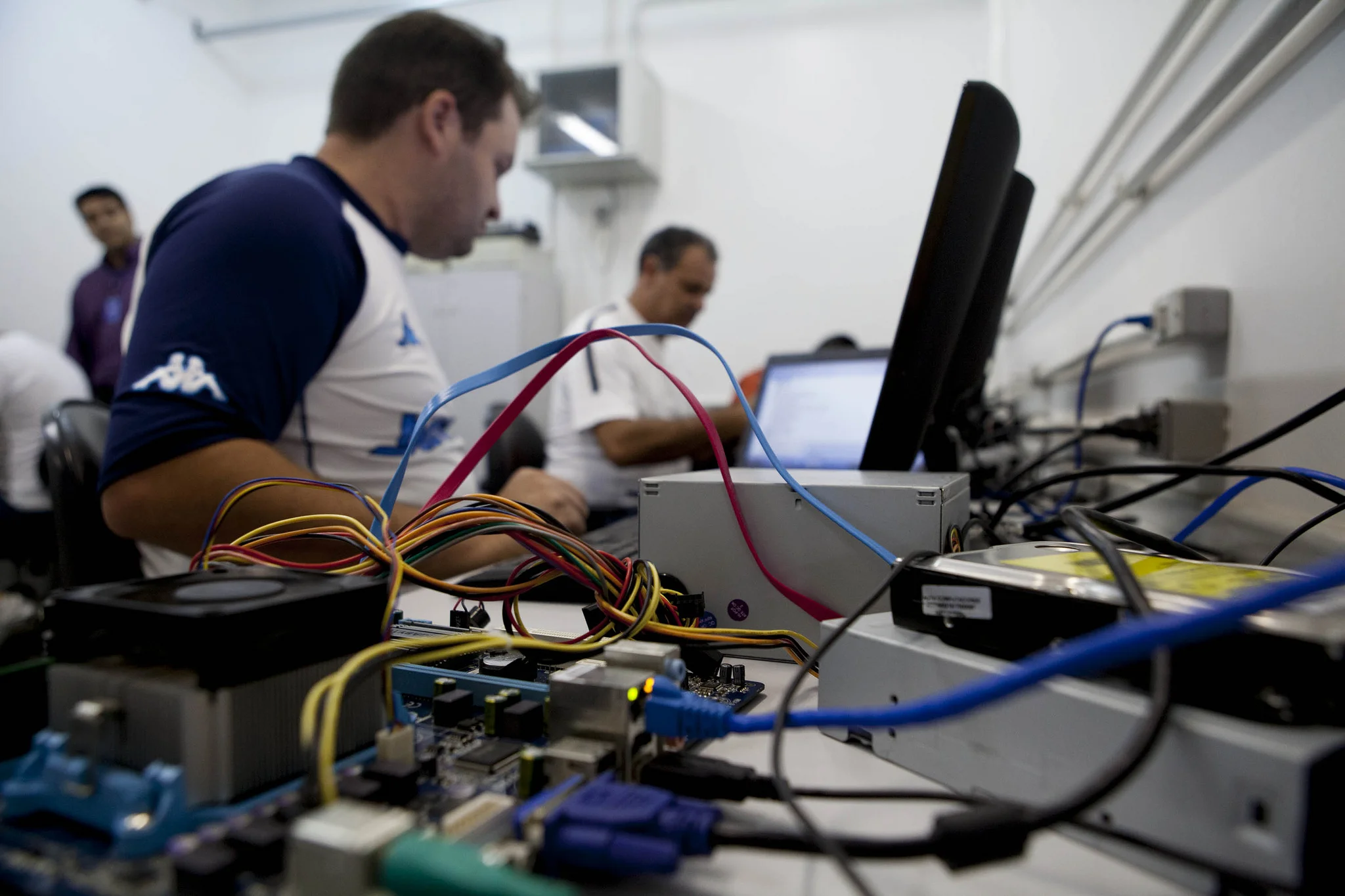 Técnicos trabalhando com equipamentos de informática, com fios e componentes visíveis em primeiro plano.