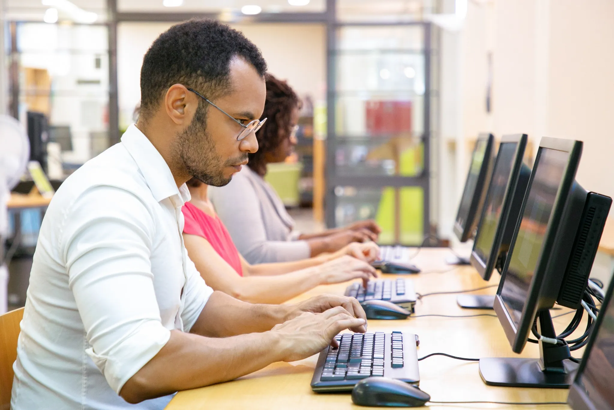 Homem concentrado digitando em computador em sala de aula moderna.