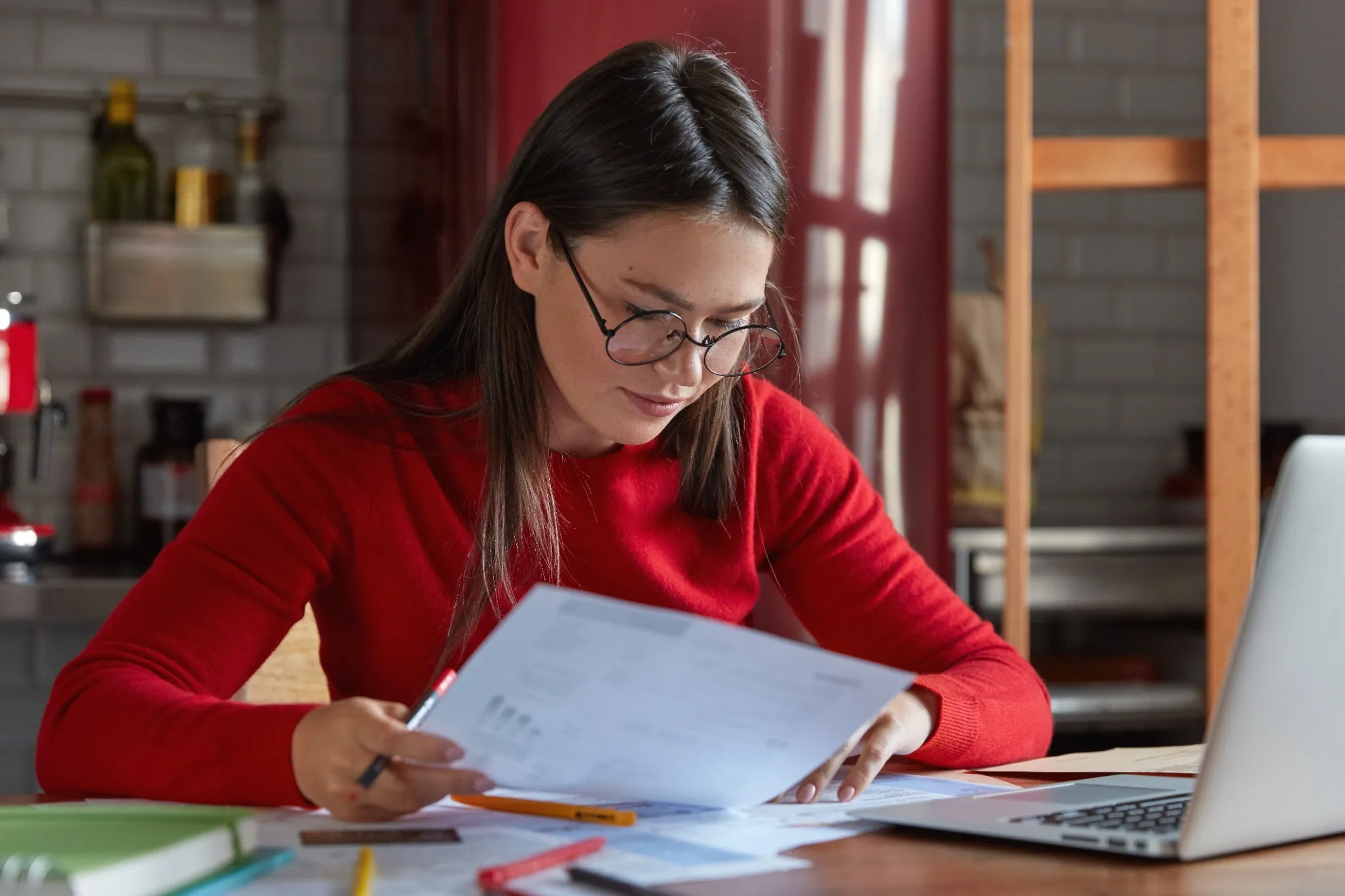 Mulher estudando e se preparando para um concurso em casa, com documentos e laptop sobre a mesa