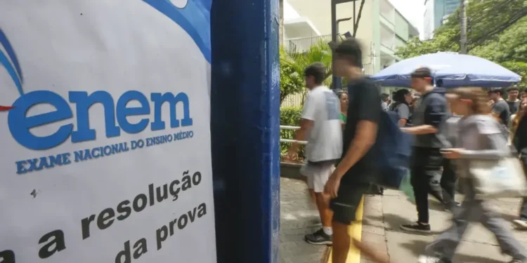 Estudantes andando em frente a um cartaz do ENEM em área urbana movimentada.