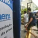 Estudantes andando em frente a um cartaz do ENEM em área urbana movimentada.