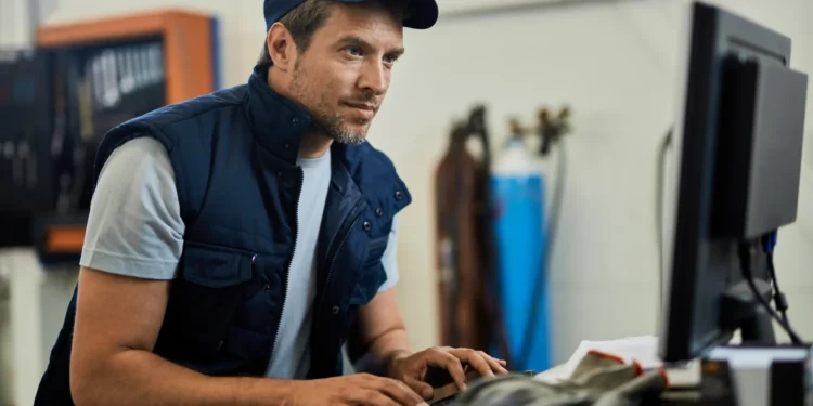 Técnico mecânico consulta informações no computador dentro da oficina