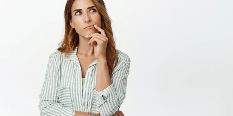 Mulher com expressão pensativa, olhando para cima, com uma mão no queixo. Ela está usando uma camisa listrada em verde e branco.