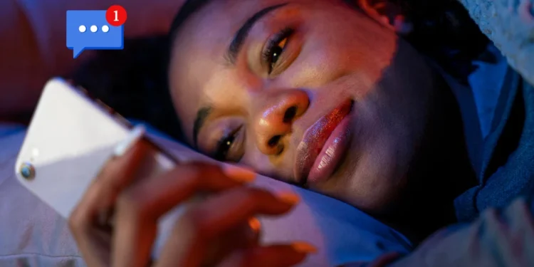 Mulher sorrindo enquanto lê uma mensagem no celular deitada na cama.