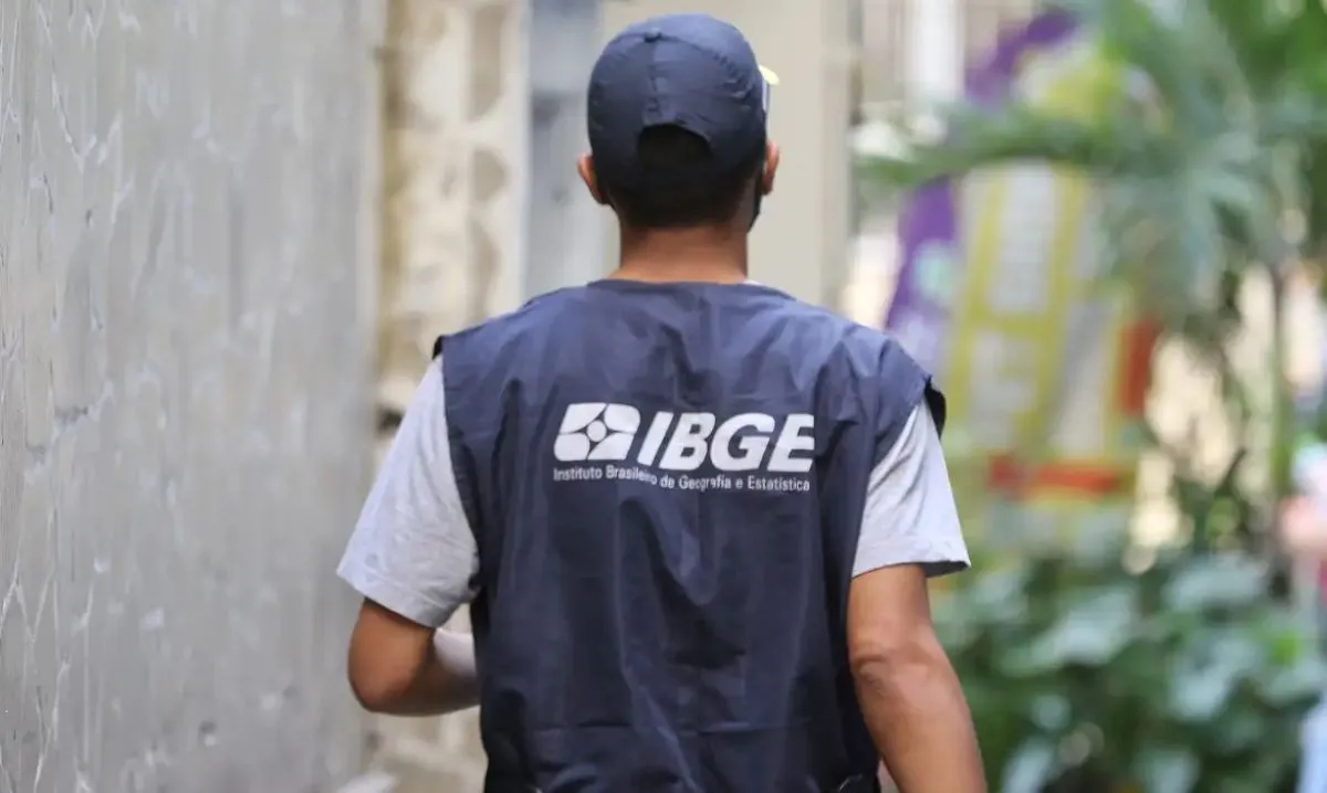 Candidato do IBGE usando uniforme enquanto realiza pesquisa de campo, representando as vagas do concurso IBGE 2025, que aguarda autorização para definir a banca organizadora.