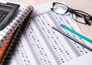 Imagem de formulário de concurso com calculadora, lápis, caderno e óculos, ilustrando a preparação para exames.