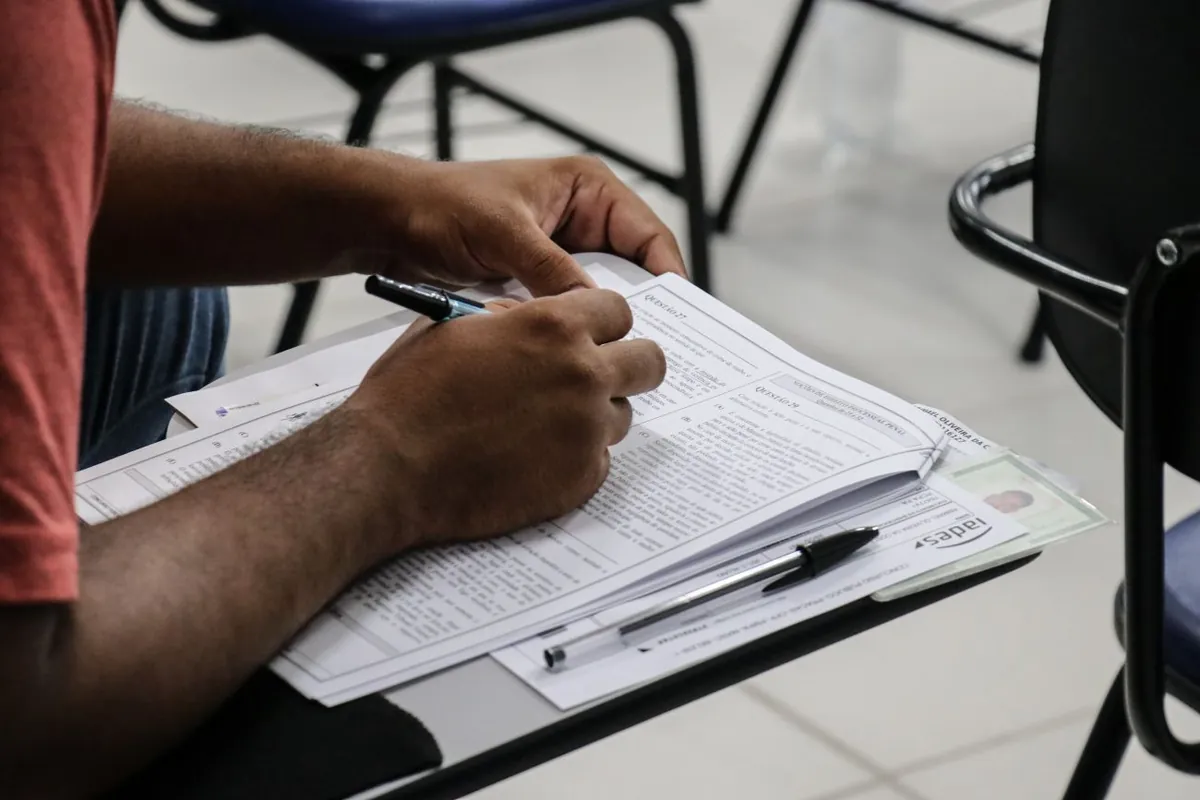 Pessoa fazendo prova objetiva em sala de aplicação de concurso.