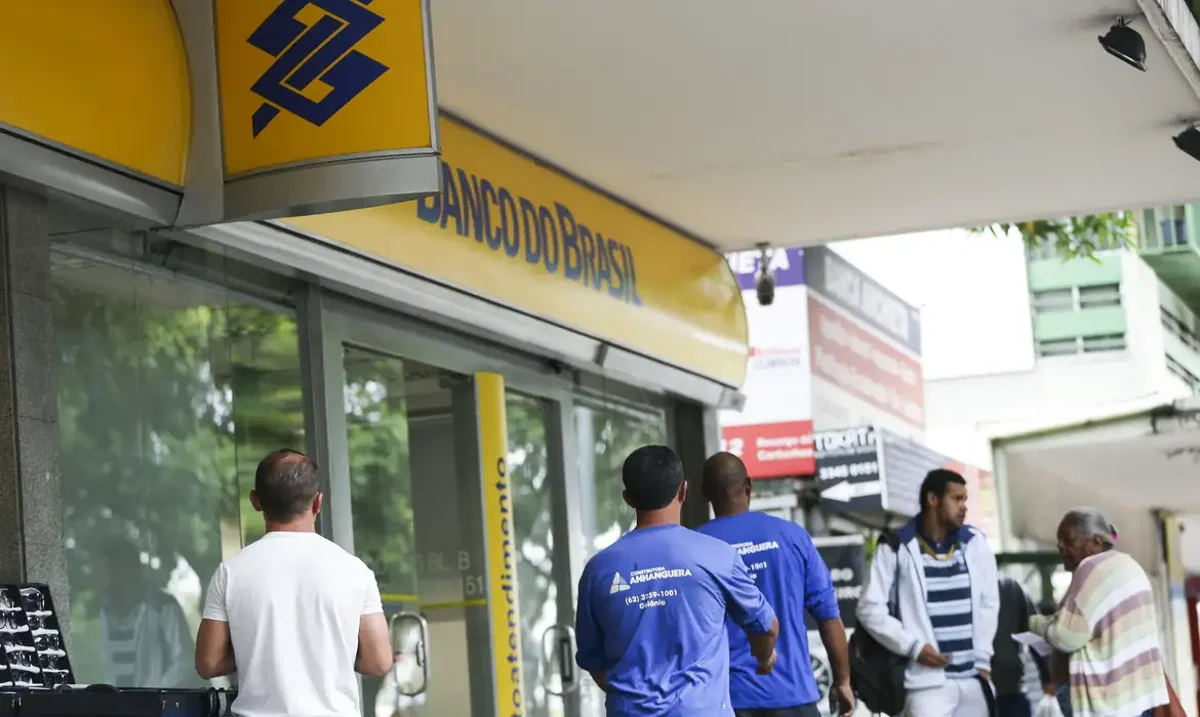 Pessoas em frente a agência do Banco do Brasil em área urbana.