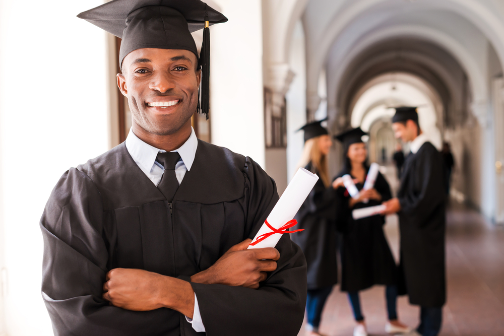 Graduação 2025: Formando sorrindo segurando diploma com colegas ao fundo, durante cerimônia de graduação
