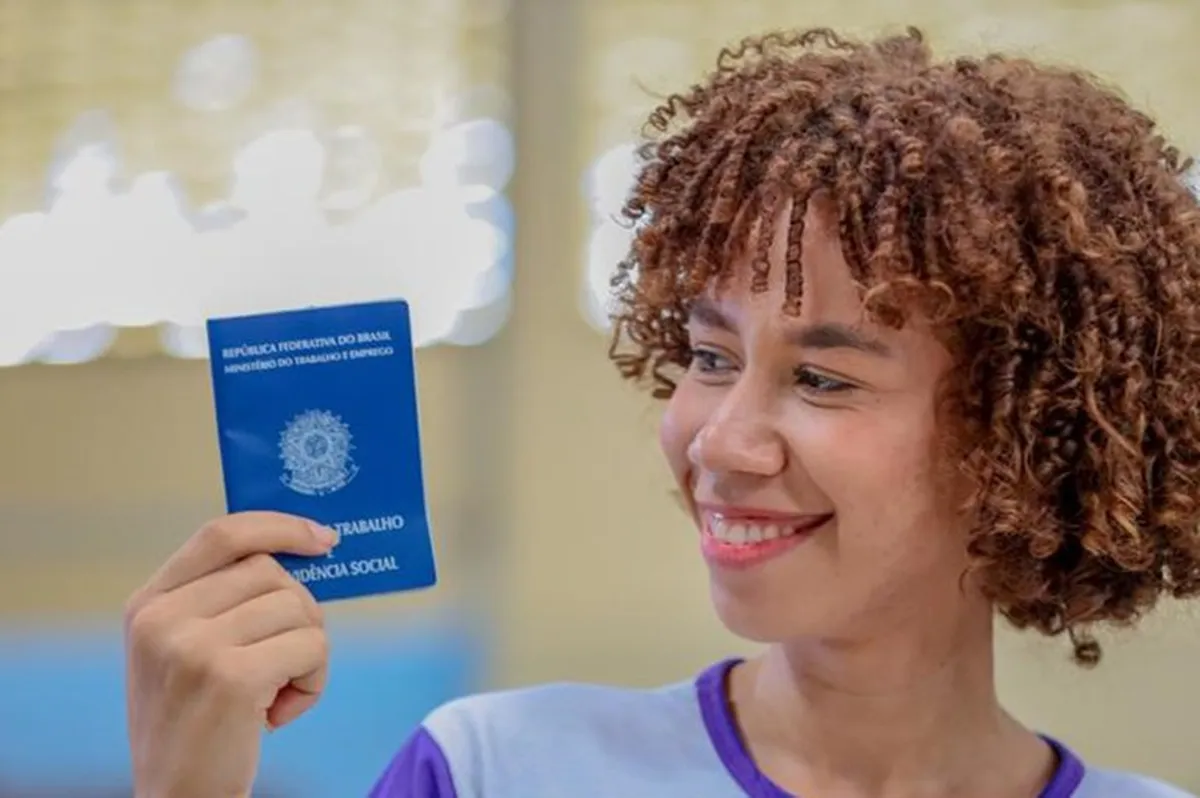 vaga de emprego no RJ: Mulher sorrindo e segurando a carteira de trabalho em um ambiente relacionado à busca de emprego.