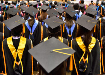 Cerimônia de formatura com alunos usando becas e capelos, vista de trás.