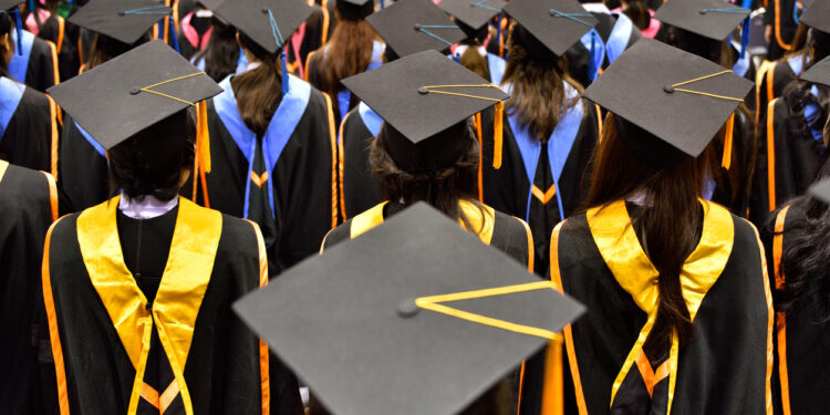 Cerimônia de formatura com alunos usando becas e capelos, vista de trás.