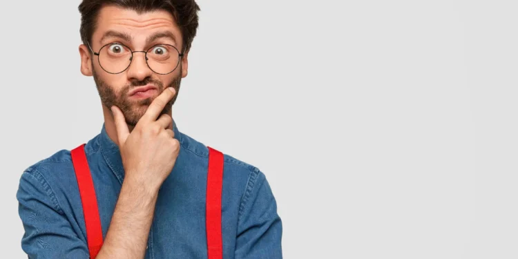 Homem com camisa jeans e suspensórios vermelhos fazendo uma expressão pensativa com os óculos.