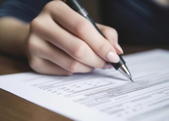 Pessoa preenchendo formulário/prova de concurso com caneta sobre uma folha de papel.