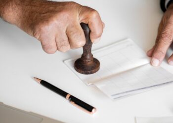 Pessoa carimbando um documento em um ambiente de trabalho de cartório. Fique atento aos concursos de cartório.