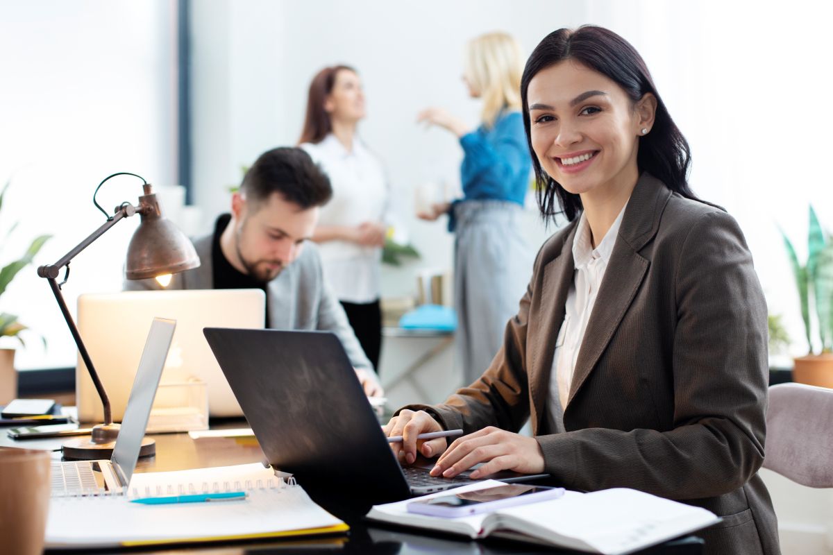 Mulher sorrindo em um escritório moderno, trabalhando em um notebook, representando o potencial de crescimento de salários em 2025.