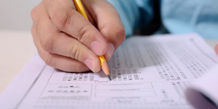 Pessoa preenchendo uma prova com um lápis em um formulário de múltipla escolha, simbolizando a prova do concurso em São Paulo.