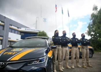 magem de policiais rodoviários federais em frente a um veículo oficial, simbolizando a carreira e os desafios da profissão.