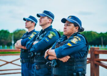 Três guardas municipais em uniforme, com braços cruzados, vigilantes e atentos em área pública. Seja você um também com o concurso Guarda Municipal.