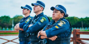 Três guardas municipais em uniforme, com braços cruzados, vigilantes e atentos em área pública. Seja você um também com o concurso Guarda Municipal.