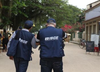 Recenseadores do IBGE em atividade, realizando trabalho de campo para o Censo 2025 em uma rua tranquila.