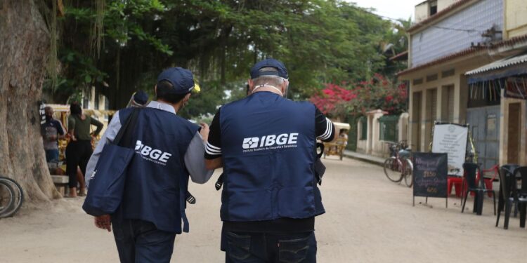 Recenseadores do IBGE em atividade, realizando trabalho de campo para o Censo 2025 em uma rua tranquila.