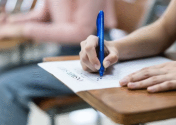 Pessoa escrevendo em uma prova com caneta azul em ambiente de sala de aula, refenciando-se ao CNU 2.