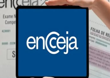 Pessoa segurando tablet com logo do Encceja, ao fundo documentos do exame nacional para jovens e adultos.