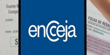 Pessoa segurando tablet com logo do Encceja, ao fundo documentos do exame nacional para jovens e adultos.