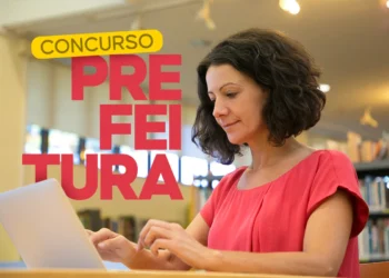 Mulher digitando em notebook em ambiente de biblioteca com anúncio de concurso da prefeitura em SP