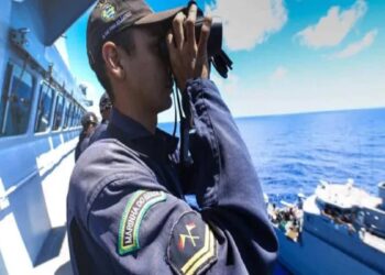 Marinheiro da Marinha do Brasil observando o mar com binóculos a bordo de um navio militar em alto mar.
