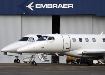 Dois jatos executivos da Embraer, o Phenom 300 e outro, estacionados em frente a um hangar da empresa.