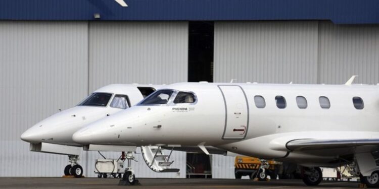 Dois jatos executivos da Embraer, o Phenom 300 e outro, estacionados em frente a um hangar da empresa.