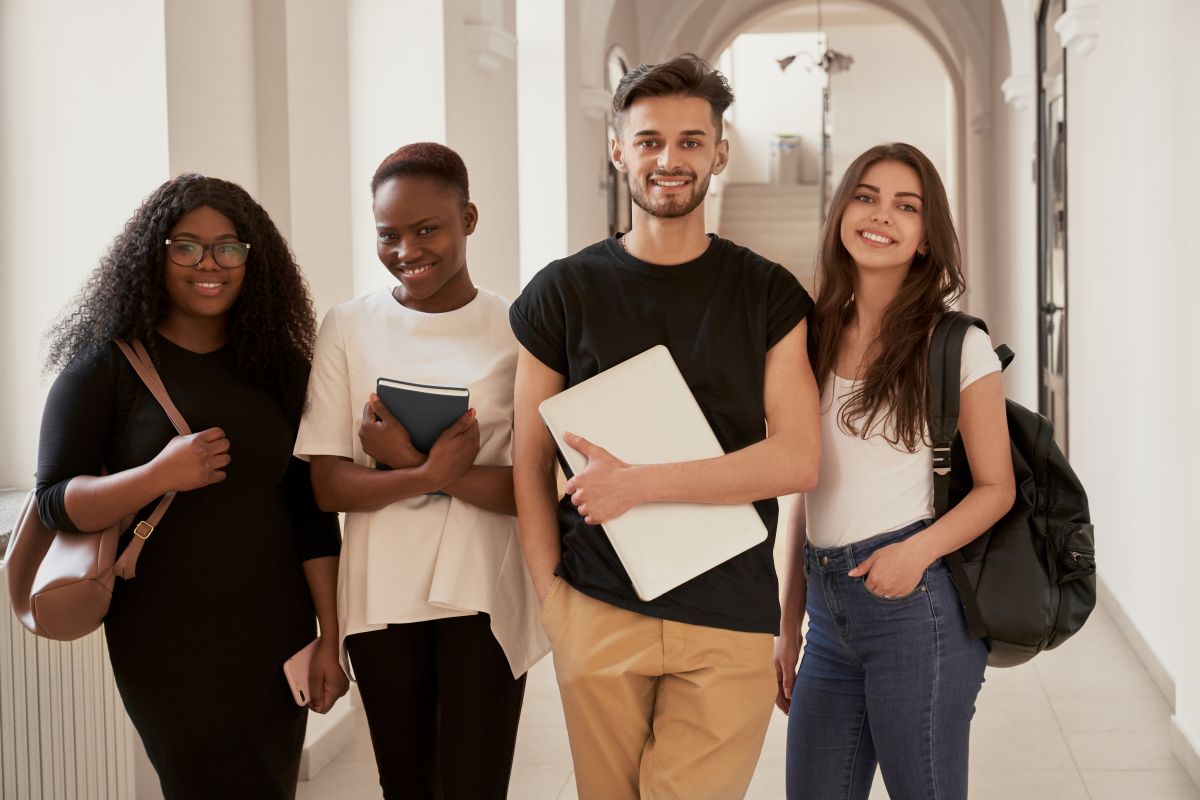 quatro universitários felizes com livros e um laptop, representando a vida acadêmica